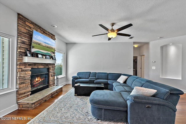 living area with a fireplace, wood finished floors, visible vents, baseboards, and a ceiling fan