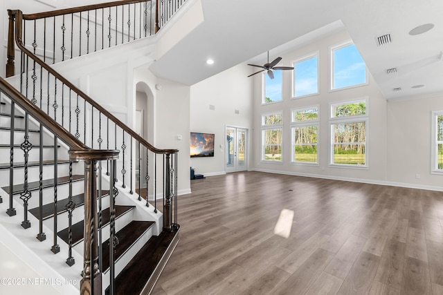 interior space featuring arched walkways, a high ceiling, ceiling fan, wood finished floors, and baseboards