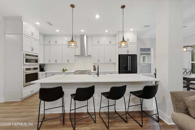 kitchen featuring high end black fridge, white cabinetry, light countertops, wall chimney range hood, and pendant lighting