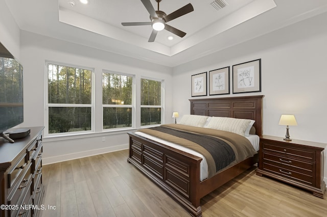 bedroom featuring light wood finished floors, a tray ceiling, visible vents, and baseboards