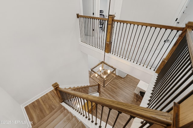 stairway featuring an inviting chandelier, baseboards, and wood finished floors