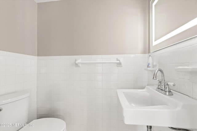 bathroom featuring wainscoting, a sink, toilet, and tile walls