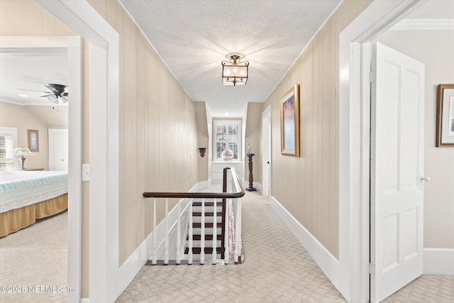 corridor with baseboards, light colored carpet, wooden walls, and an upstairs landing