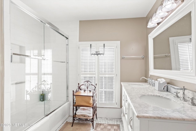 bathroom with double vanity, bath / shower combo with glass door, plenty of natural light, and a sink