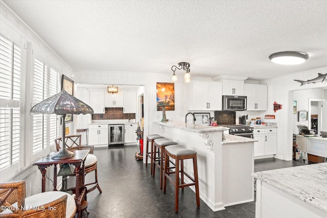 kitchen with beverage cooler, stainless steel appliances, light stone counters, and white cabinetry