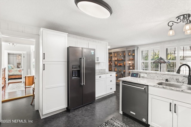 kitchen with white cabinets, light stone countertops, stainless steel appliances, a textured ceiling, and a sink