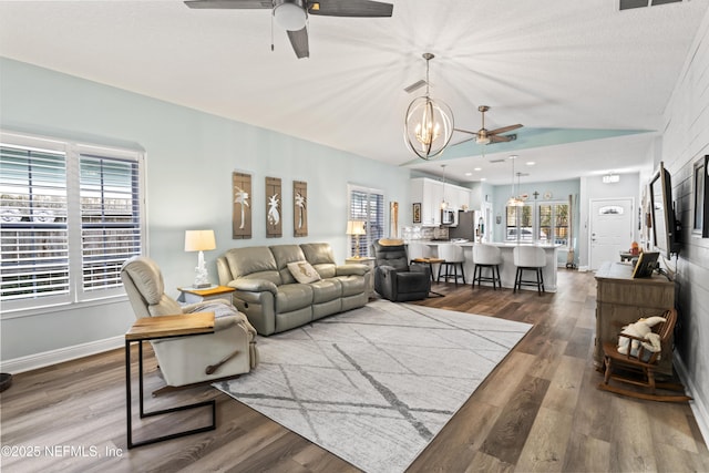 living room with vaulted ceiling, ceiling fan with notable chandelier, wood finished floors, and baseboards