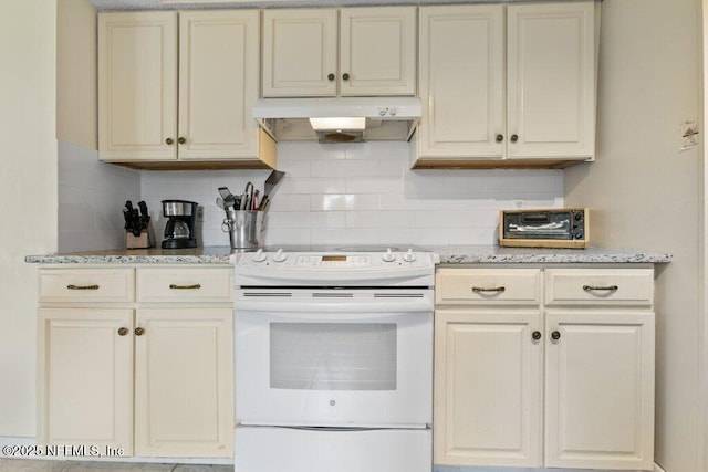 kitchen featuring electric range, light stone counters, cream cabinets, under cabinet range hood, and backsplash