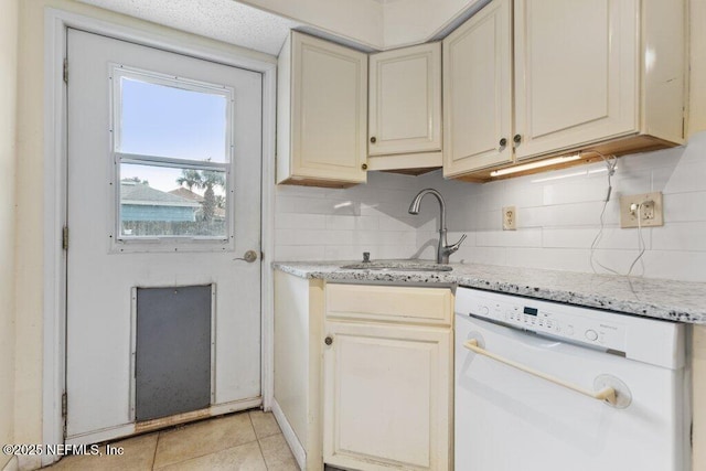 kitchen featuring backsplash, cream cabinets, white dishwasher, a sink, and light stone countertops