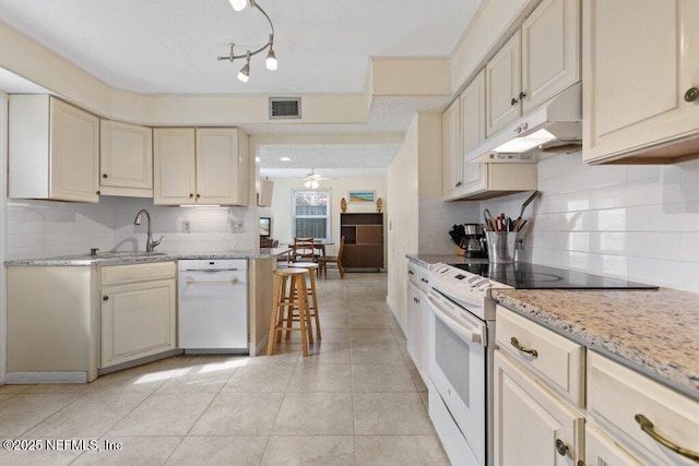 kitchen featuring cream cabinetry, visible vents, a sink, white appliances, and under cabinet range hood