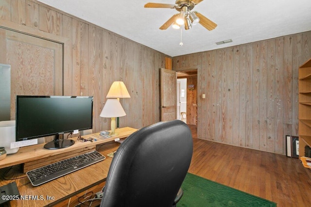 office space with wood walls, wood finished floors, visible vents, and a ceiling fan