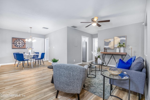 living area with light wood-style floors, baseboards, visible vents, and ceiling fan with notable chandelier