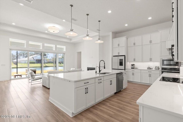 kitchen featuring light wood finished floors, white cabinets, an island with sink, stainless steel appliances, and a sink