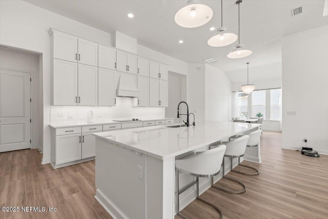 kitchen featuring white cabinets, custom exhaust hood, black electric cooktop, and a sink