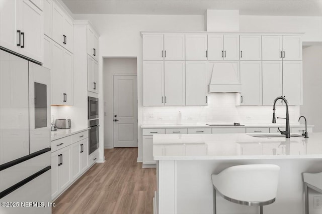 kitchen featuring black electric stovetop, oven, a sink, backsplash, and custom exhaust hood