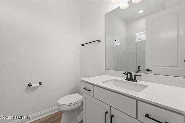 bathroom with toilet, wood finished floors, vanity, baseboards, and a tile shower