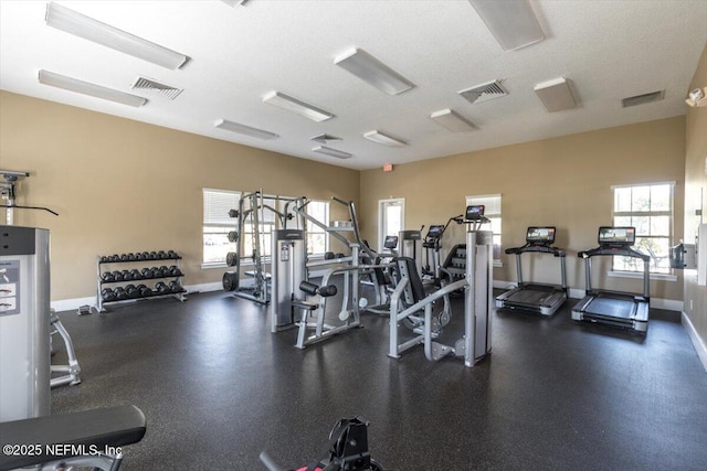 exercise room with a textured ceiling, visible vents, and baseboards