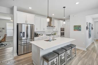 kitchen with a sink, white cabinets, appliances with stainless steel finishes, wall chimney range hood, and a center island with sink