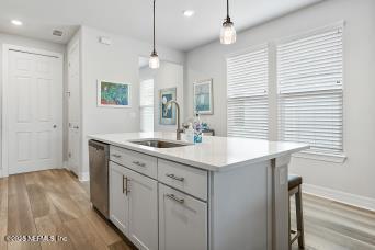 kitchen featuring hanging light fixtures, dishwasher, light wood-style floors, and a sink