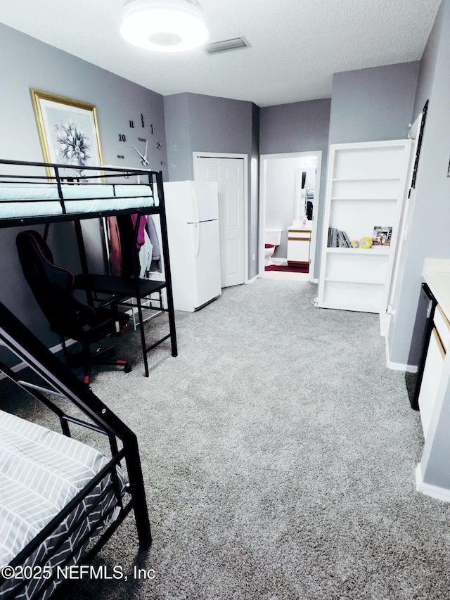 carpeted bedroom with a textured ceiling, freestanding refrigerator, and baseboards