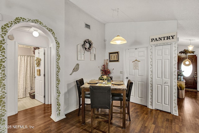 dining space featuring dark wood-style floors, arched walkways, visible vents, and lofted ceiling