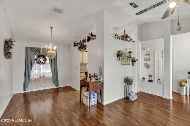 foyer entrance with dark wood-style floors, vaulted ceiling, ceiling fan with notable chandelier, and visible vents