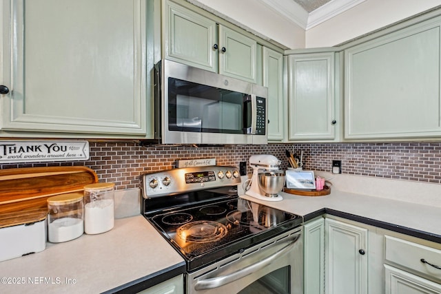 kitchen featuring green cabinetry, decorative backsplash, light countertops, appliances with stainless steel finishes, and crown molding