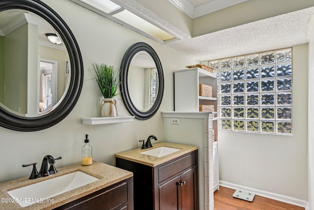 full bath featuring two vanities, wood finished floors, baseboards, and a sink