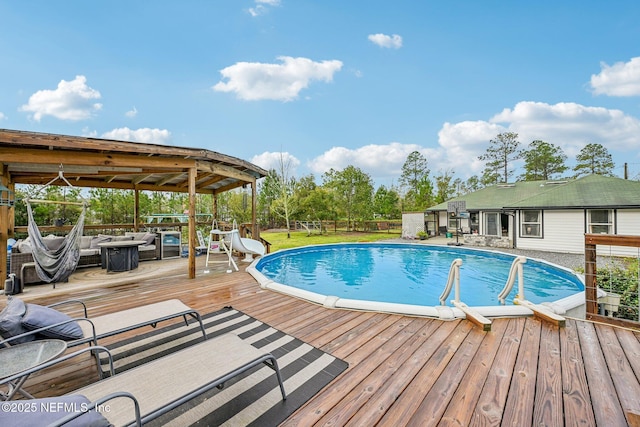 pool with a wooden deck, a water slide, and fence