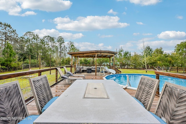 outdoor pool featuring outdoor dining space, a yard, a water slide, and a wooden deck