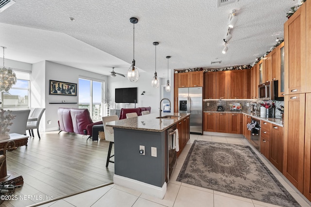 kitchen with brown cabinets, decorative light fixtures, a breakfast bar area, stainless steel appliances, and a kitchen island with sink