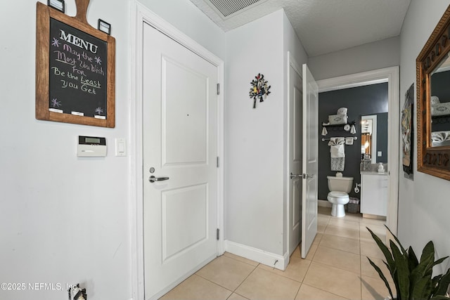 hallway featuring light tile patterned floors, visible vents, baseboards, and a textured ceiling