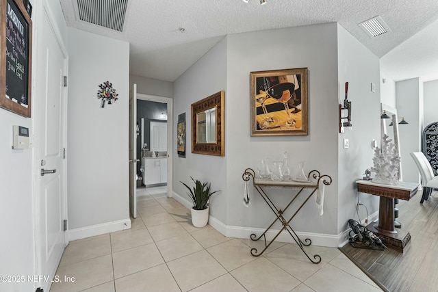 corridor featuring visible vents, a textured ceiling, and light tile patterned flooring