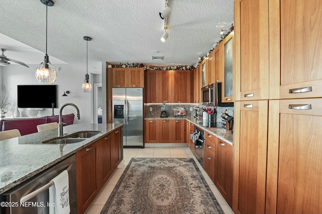 kitchen with brown cabinetry, glass insert cabinets, appliances with stainless steel finishes, light stone counters, and a sink