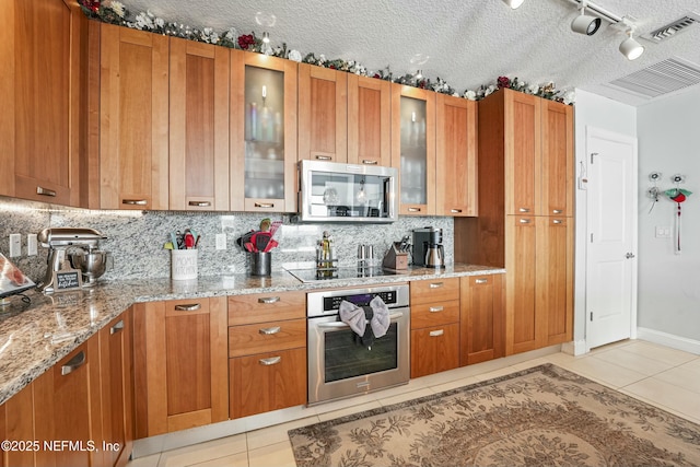 kitchen featuring stainless steel appliances, brown cabinetry, glass insert cabinets, and visible vents