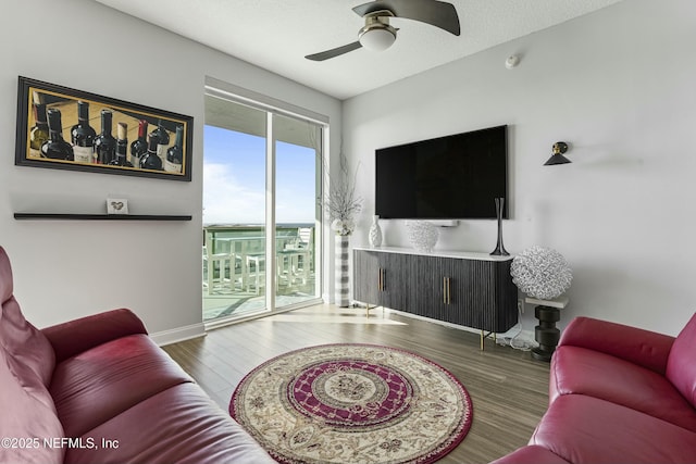 living room with ceiling fan, a textured ceiling, baseboards, and wood finished floors