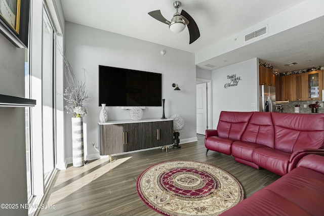 living room featuring baseboards, visible vents, a ceiling fan, dark wood-style flooring, and a textured ceiling