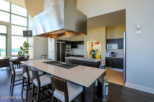 kitchen with island range hood, a high ceiling, paneled built in fridge, a center island with sink, and stainless steel gas stovetop
