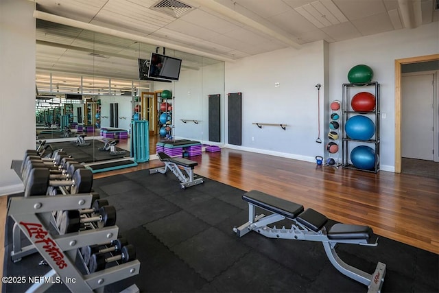 exercise room with baseboards, visible vents, and wood finished floors