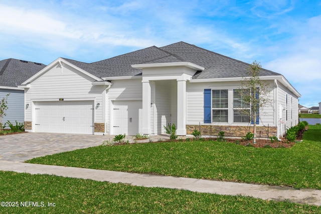 view of front of property with stone siding, a shingled roof, decorative driveway, and a front yard