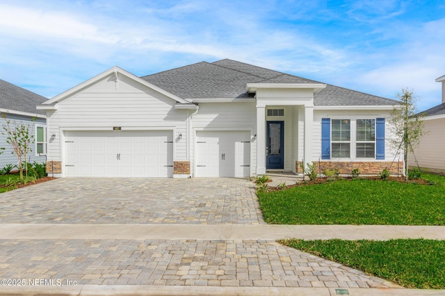 view of front of home with a garage, roof with shingles, a front lawn, and decorative driveway