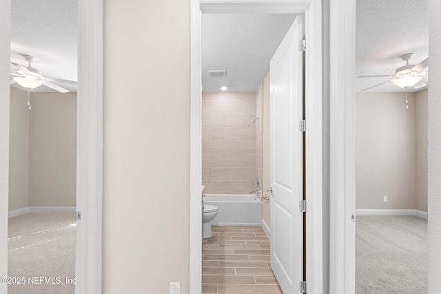 hallway with baseboards, visible vents, a textured ceiling, and light colored carpet