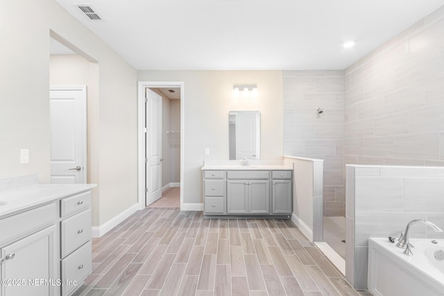 full bathroom featuring baseboards, visible vents, a garden tub, walk in shower, and vanity