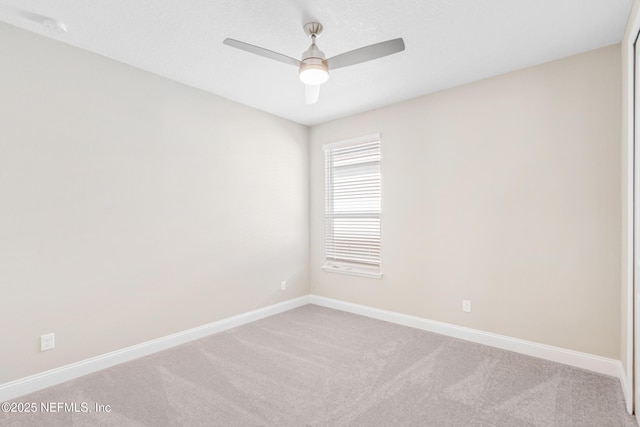 spare room featuring light colored carpet, ceiling fan, and baseboards