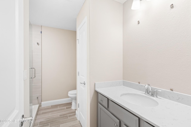 bathroom featuring toilet, vanity, baseboards, wood tiled floor, and a stall shower