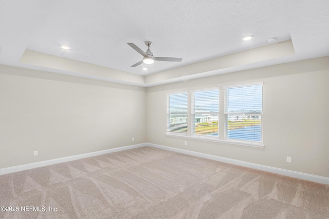 unfurnished room with light carpet, a tray ceiling, and baseboards