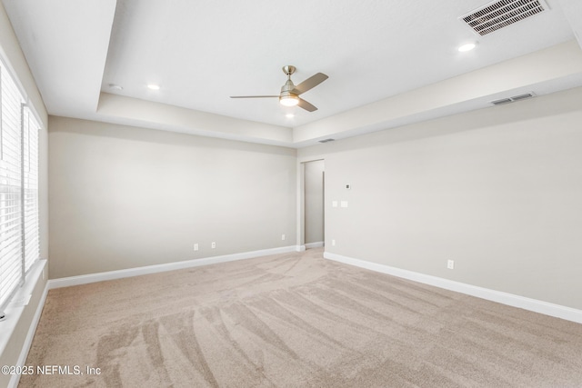 spare room with a tray ceiling, visible vents, and baseboards