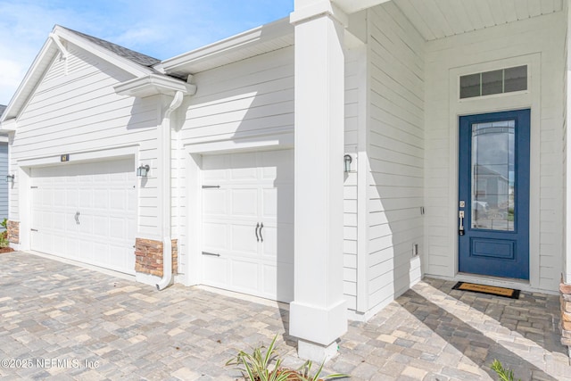 view of exterior entry with a garage and decorative driveway