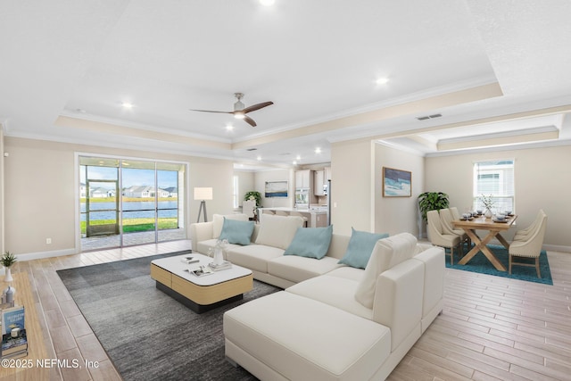 living area with visible vents, baseboards, ornamental molding, wood tiled floor, and a tray ceiling