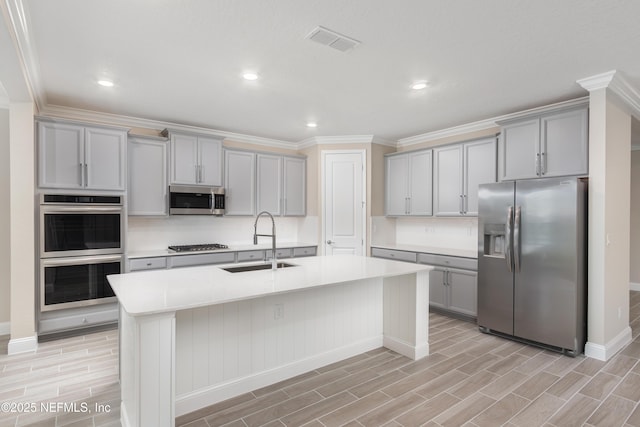 kitchen with stainless steel appliances, light countertops, visible vents, a kitchen island with sink, and a sink